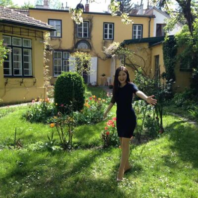 初夏の陽光が差し込むウィーンの庭園に立つ田中彩子さん