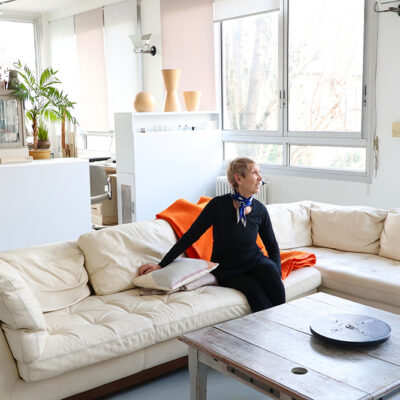 北マレの明るいアパルトマンのリビングで、白いソファに腰掛けるアクセサリーデザイナーのアンナ・カゼルさん