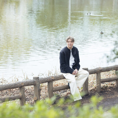 都立石神井公園の池のそばの柵に腰を下ろしているアートディレクター中田嘉生さん