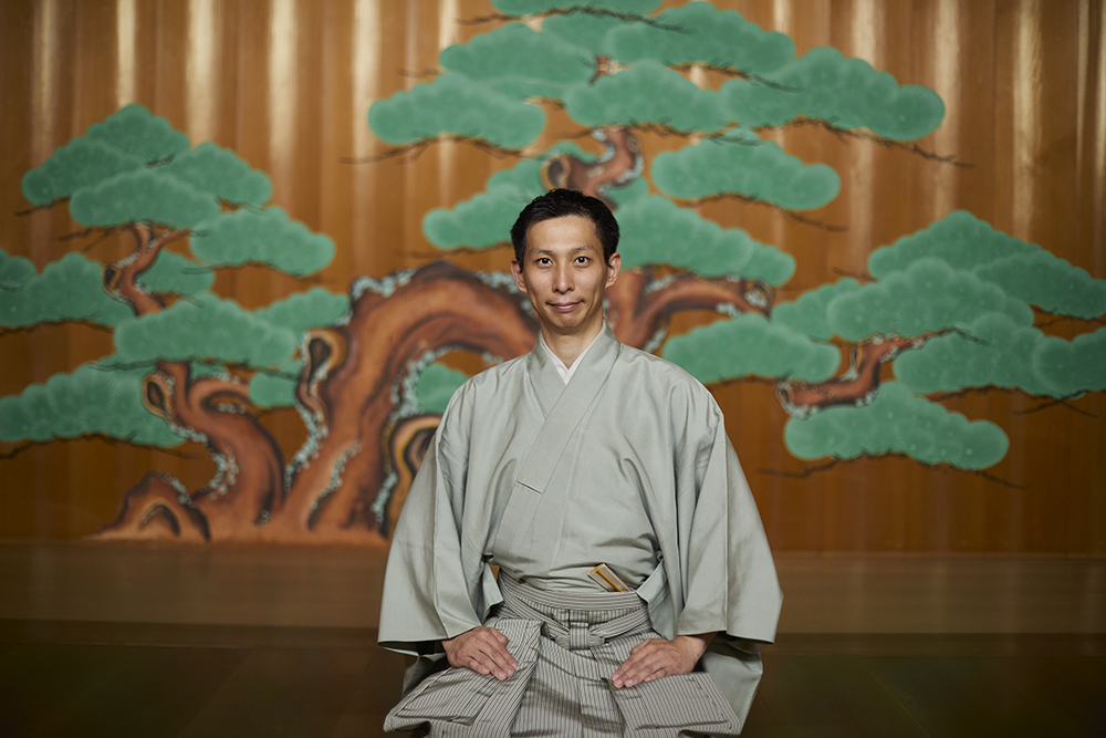 能舞台を背景に佇む能楽師・塩津圭介さん