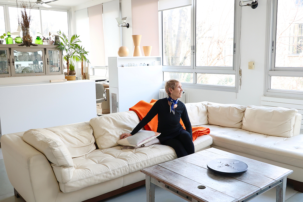北マレの明るいアパルトマンのリビングで、白いソファに腰掛けるアクセサリーデザイナーのアンナ・カゼルさん