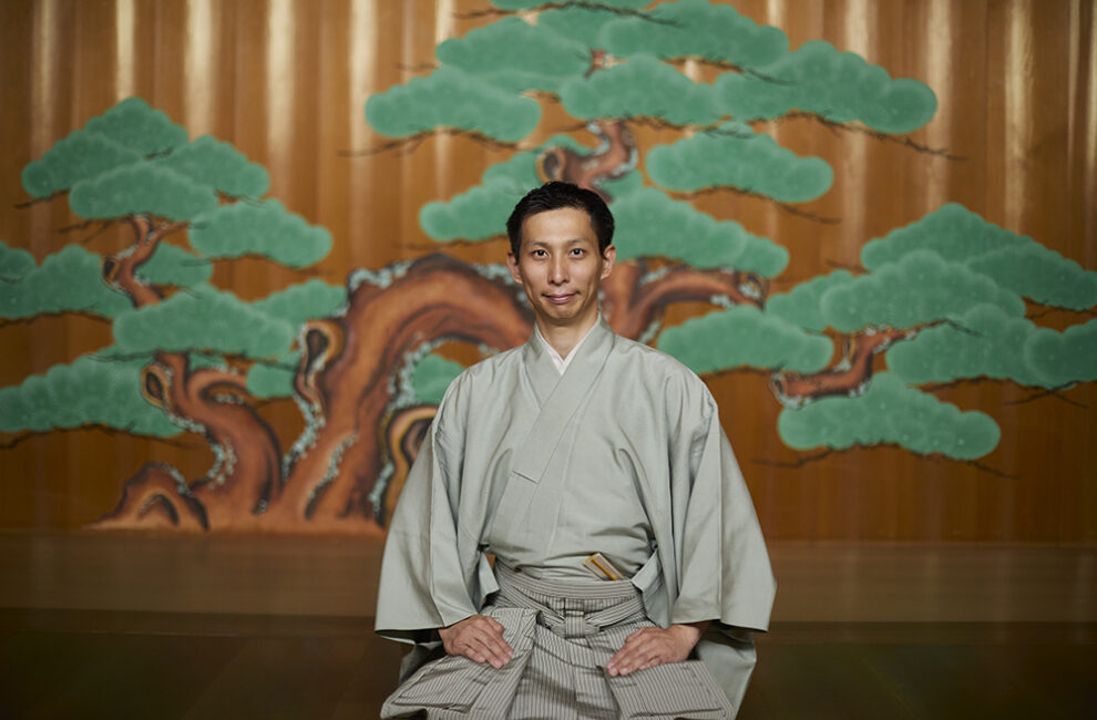 能舞台を背景に佇む能楽師・塩津圭介さん